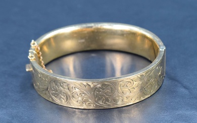 A 9ct gold hinged bangle having engraved scroll decoration, safety chain broken, inner diameter 62mm