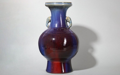 A CHINESE FLAMBÉ-GLAZED VASE. Qing Dynasty. The ovoid body with two plain bands to the shoulder rising to a waisted neck framed by two elephant head handles, all supported on a tall flared foot and decorated with a maroon glaze with lavender...