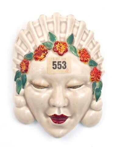 A Clarice Cliff Marlene face mask wall pocket, the beige glazed face with red painted lips and red and green floral headband, 17cm high (AF) (VAT charged on hammer price)