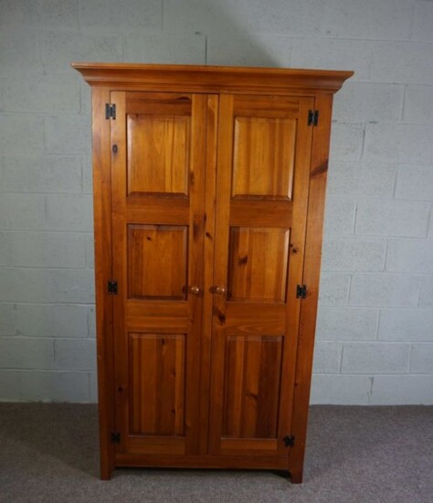 A modern varnished pine wardrobe, fitted with two panelled doors enclosing drawers and a hanging