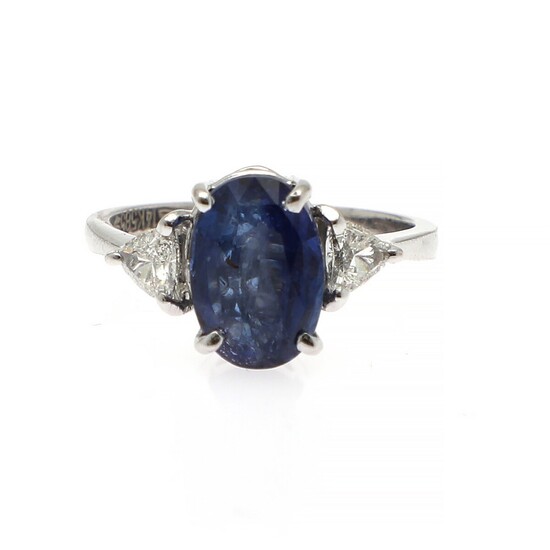 A sapphire and diamond ring set with an oval-cut sapphire flanked by two trilliant-cut diamonds, mounted in 14k white gold. Size 52.5.