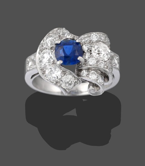 A Sapphire and Diamond Cluster Ring, the central round cut sapphire in a white claw setting, within