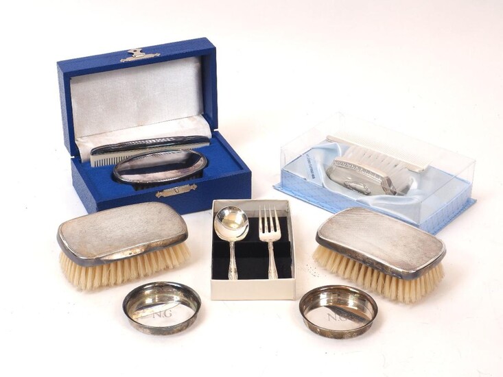 A pair of silver backed brushes, London, c.1974, TP, the engine turned backs with presentation engraving to sides, together with two silver ashtrays; a spoon and fork Christening set, stamped sterling; a comb and brush set, stamped sterling, and a...