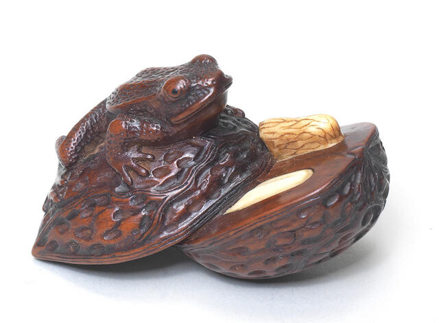 A wood netsuke of a frog on a split walnut