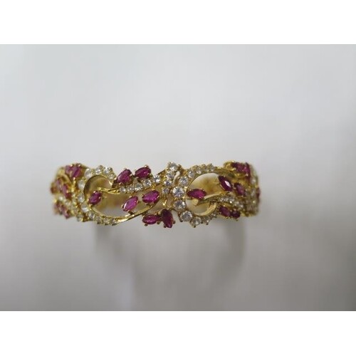 A yellow gold ruby and white stone hinged bangle, tests to a...