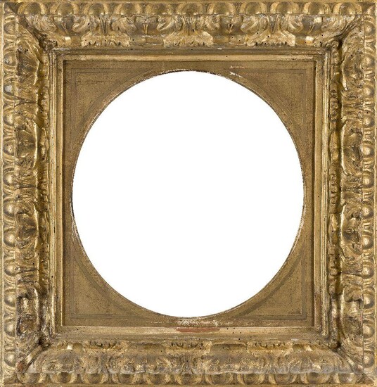 An Italian Carved and Gilded Leaf Frame, 18th century, with hand-tooled spandrels and tondo aperture, ovolo sight, the top knull with scrolling leaf and shield in high relief and egg-and-dart back edge, 39 cm. diameter (sight).