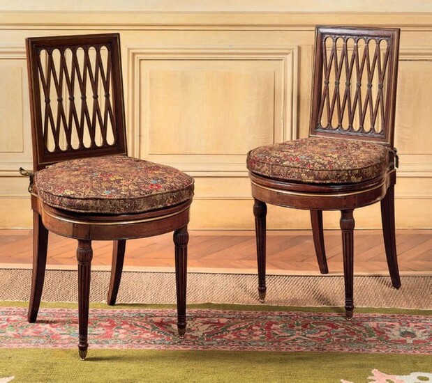Pair of mahogany moulded and carved chairs, chiselled and gilded brass ornamentation, the seat with cane bottom, the flat openwork backrest with crossbars decoration, the tapered and fluted legs finished with casters.