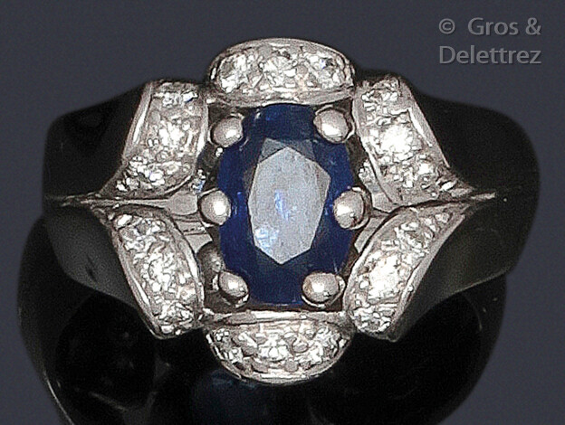 Ring " Fleur " in white gold, adorned with an oval sapphire facetted in dome-shaped surrounds set with brilliant-cut diamonds forming the petals. Work from the 1950s. Tour of doigt : 53. P. Brut : 9.1 g.