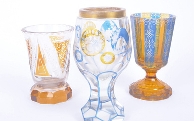A collection of three early 20th Century Czech wine glass goblets in the manner of Moser. Each being decorated with carved cameos depicting buildings & flowers, another in citrine glass with blue flash panels along with an engraved clear glass example...