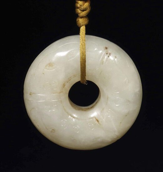jade pendant China, probably early Qing Dynasty, light seladon-coloured jade, ring-shaped pendant with broad, rounded walls, flat reliefed taotie and curlicue decoration in archaic style, on silk ribbon with carnelian bead, d: approx. 5,5 cm.