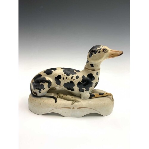 A Staffordshire figure of a recumbent black and white greyho...