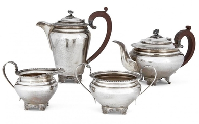 A four-piece silver tea set by Garrard & Co., Birmingham, c.1964, comprising tea pot, coffee pot, sugar and milk jug, each with gadrooned rim and raised on four wing-shouldered paw feet, the pots with wooden handles and flower finials to hinged...