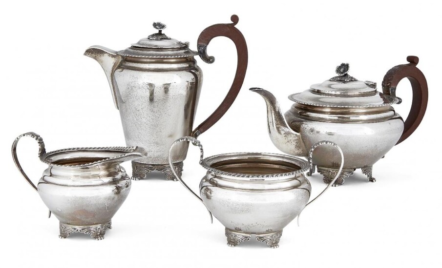 A four-piece silver tea set by Garrard & Co., Birmingham, c.1964, comprising tea pot, coffee pot, sugar and milk jug, each with gadrooned rim and raised on four wing-shouldered paw feet, the pots with wooden handles and flower finials to hinged...