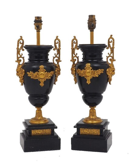 A pair of French slate gilt metal mounted urn-form table lamps, early 20th century, with mask and scroll handles raised on stepped square base set with a plaque depicting a classical scene, 41cm high to fitting