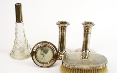 A pair of hallmarked silver candlesticks, a circular silver photo frame, silver backed brush and a silver mounted perfume bottle.
