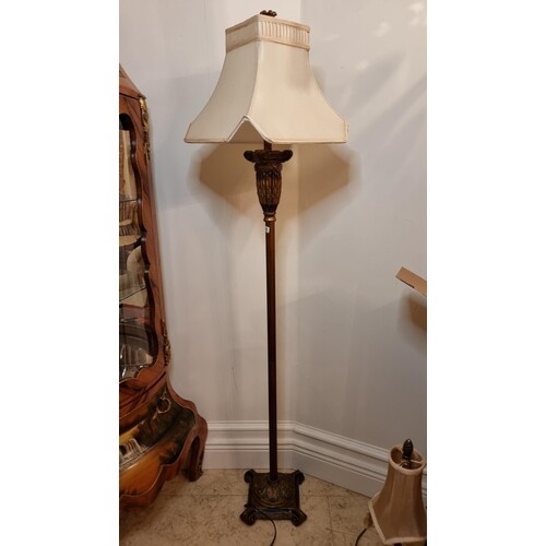 A tall standing floor lamp in dark brass tone with classical...