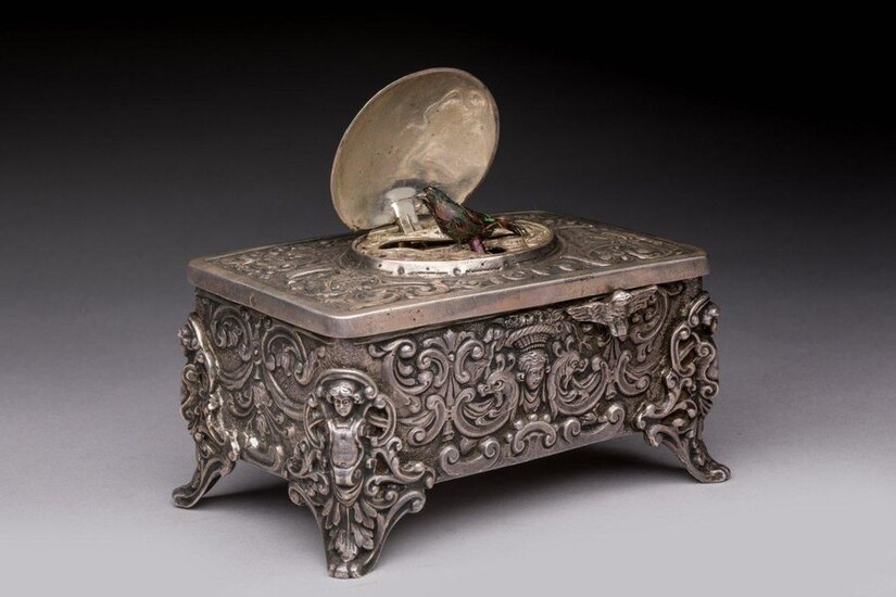 AUTOMATIC MUSIC BOX with BIRD BIRD in silver. On the lid, a medallion engraved in relief of a head carrying a flowery basket, in a frame of bird couples at the fountain, opens to discover an automaton bird adorned with natural feathers. The front...