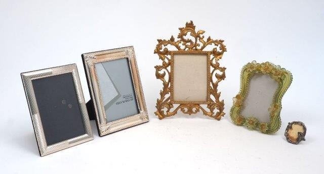 A group of five photo frames comprising: two silver plated rectangular examples (12.9 x 18cm and 14.7 x 19.8cm); a green acrylic example with applied flowerheads, 13.5 x 17cm; a gilt metal example with foliate scroll border, 19 x 26cm; and a...