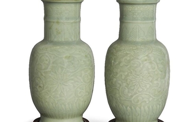 A pair of Chinese celadon-glazed carved 'lotus' vases, late Qing dynasty, the exteriors decorated with flowering lotus blossom issuing from leafy stems beneath bands of ruyi lappets, covered in an allover celadon glaze, underglaze blue apocryphal...