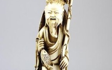 Fisherman with child, ivory figure, China circa 1920, figure carved from one piece, deepenings rubbed out with dark brown paint, standing figure of a fisherman with rod, basket and several fish, at his side a child, on square wooden base, h without...