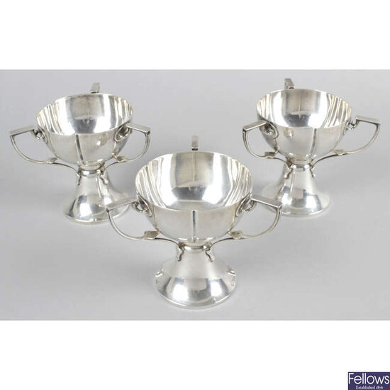 Three Edwardian silver pedestal cups, in Art Nouveau style, each with three handles. (3).