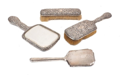 Two Victorian silver backed brushes and a hand mirror, Birmingham, c.1896 and 1897, Henry Matthews, the reverse of all three items richly decorated with scroll, flower and foliate motifs, vacant cartouches to centre of each, together with the...