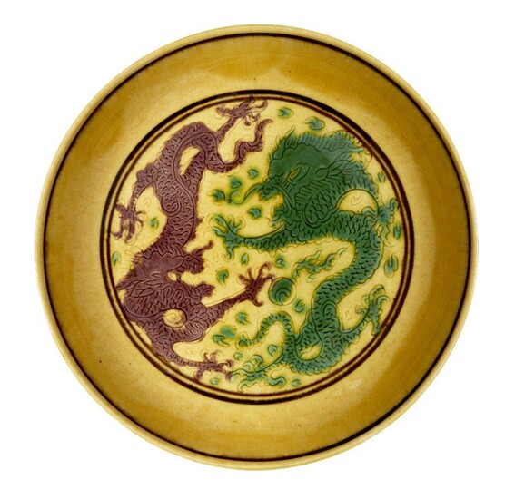 A Chinese yellow-ground aubergine and green-decorated saucer dish, Kangxi mark and of the period, incised to the central medallion with two five-clawed dragons chasing the flaming pearl, painted to the exterior with four bunches of grapes...