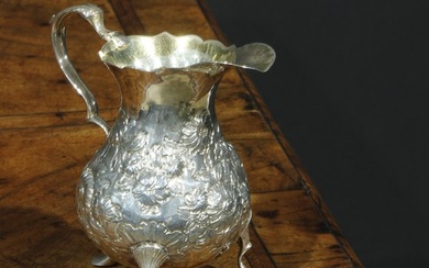 A George III silver bellied cream jug, chased with flowers a...