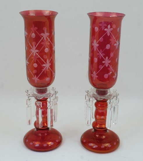 A pair of cranberry glass lustre candlestick lamps, 20th century, with clear glass sconces and faceted drops, some missing, the knopped stems atop rounded circular bases, with bell form shades etched with circle and four leaf flowers arranged in a...