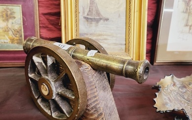 A solid brass cannon on wheels and a wooden base. 26cm long
