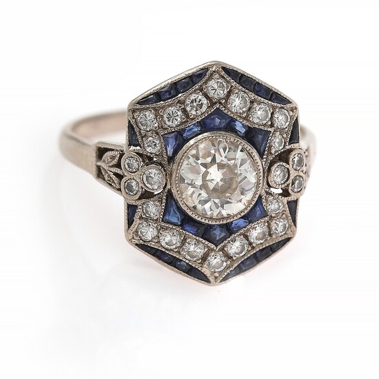 An Art Deco sapphire and diamond ring set with a diamond weighing app. 0.80 ct. encircled by numerous diamonds and sapphires, mounted in platinum. Size 54.