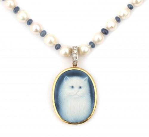 A cameo pendant with a gold mount suspended by a pearl necklace. A cultured pearl necklace with sapphire spacer beads to a 14 karat gold clasp. The agate cameo, depicting a cat has a brilliant set bale. Signed by Hans Ulrich Pauly, Idar-Oberstein...