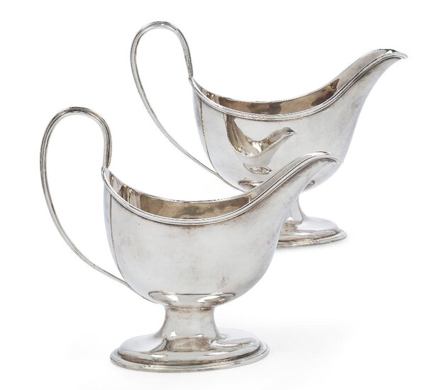 A pair of George III silver pedestal sauce boats, London, 1783, Hester Bateman, each designed with reeded handle and raised on a stepped oval foot, engraved with identical crests beneath spouts, 14.5 and 15cm high, 18cm long (inc. handles), total...