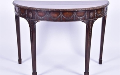 A late Victorian carved walnut demi lune table the top with leaf pattern rim above a frieze with ribbon swags supported...
