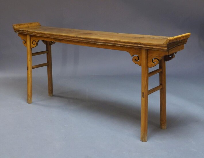 A Chinese elm altar table, 20th Century, the rectangular top with raised ends above frieze with carved scrolling decoration, on cylindrical, 89cm high, 197cm wide, 38cm deep