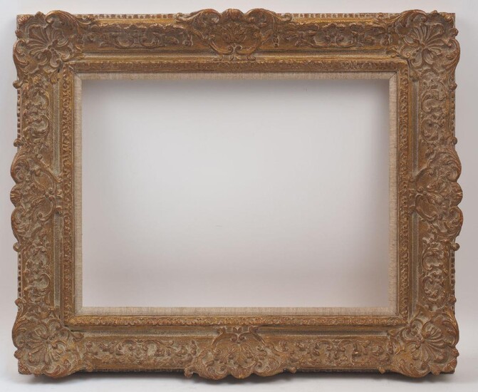A Gilded Composition Louis XIV transitional Style Frame, 20th century, with added linen mounted slip, ovolo sight, stiff leaf, sanded frieze, the ogee with foliate and flower head scrollwork and leaf cartouche centres and palmette shell cartouche...