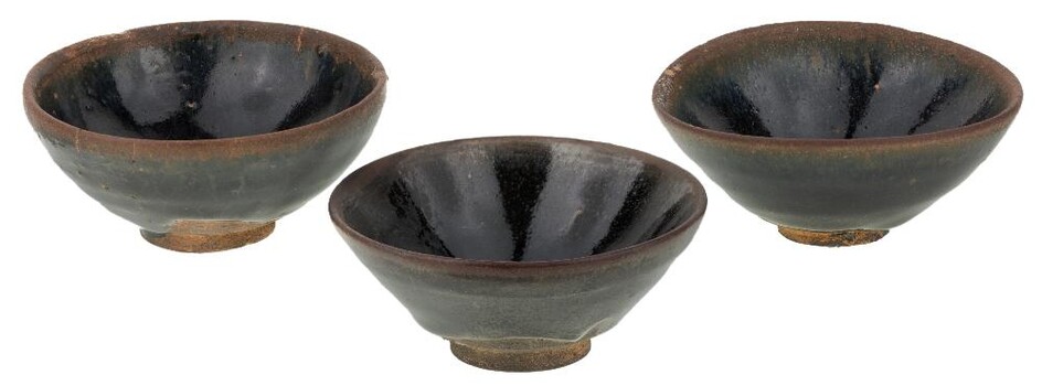 A group of three Chinese Jian ware tea bowls, Song dynasty, each of conical shape with deep sides rising from a short foot, covered in black glaze with hare fur pattern to rim, 9.2cm - 9.5cm diameter. (3) 宋 建盞一組三件