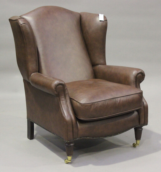 A modern brown leather wing back armchair by Laura Ashley, raised on fluted legs and brass castors