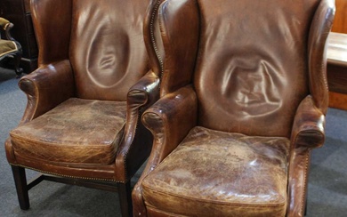 A pair of Georgian style brown leather wingback armchairs