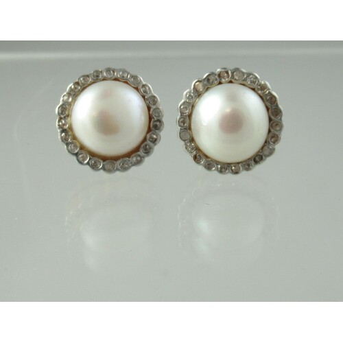A pair of cultured pearl and diamond earrings. The half pea...
