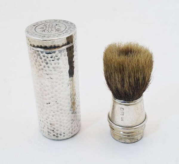 A silver cased travelling shaving brush, London, 1908, of planished cylindrical form with monogram to hinged top, the silver mounted brush is stored inside the tube and screwed to the body for use, 8cm high, weighable silver approx. 2.3oz