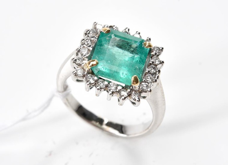 AN EMERALD AND DIAMOND CLUSTER RING-Centrally set with an emerald cut emerald weighing 3.10cts, surrounded by round brilliant cut di...