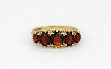An early 9ct yellow gold ring set with oval cut graduated garnets, (O).