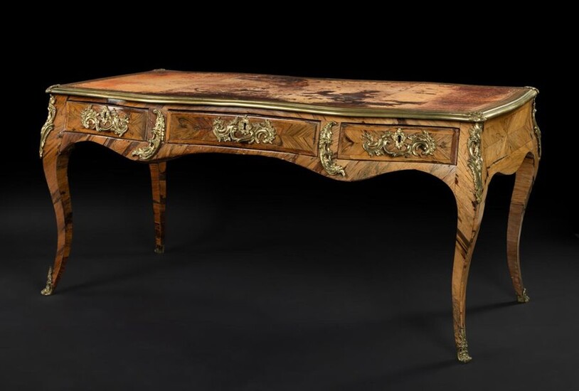 Large flat rosewood desk with an animated shape, opening with three drawers, resting on arched legs with gilded bronze foliage scrolls.