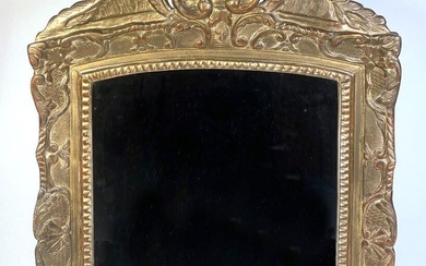 Miroir biseauté dans un cadre en bois doré et sculpté. Le fronton surmonté d'une coquille....