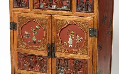 Petit meuble en bois sculpté, laqué rouge, noir et or à décor de "Personnages" et incrusté de jade ouvrant par un tiroir et deux portes pleines. Travail chinois. Epoque: vers 1900. Dim.:+/-66,8x95x44,7cm.