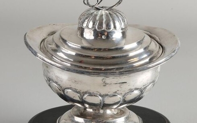 Silver tobacco jar, 833/000, oval model with fluting on oval base with a lid with fluting and swirl, flower is missing. The whole is placed on an oval black wooden base. MT .: Alexander Mentz Leeuwarden, 1843-1856. 16x13x18cm. Edge slightly out of...