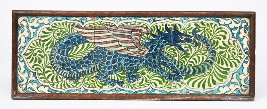 A William De Morgan Dragon three tile panel, the dragon modelled standing its tail wrapped back around its body, on foliate panel ground, in shades of blue, green, turquoise and aubergine on a white ground, framed, damages, 20.5cm. square