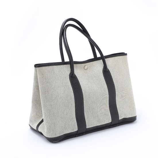 Hermès: A “Garden Party Tote Bag” of beige canvas and black leather with a large compartment with button closure, and two leather handles.