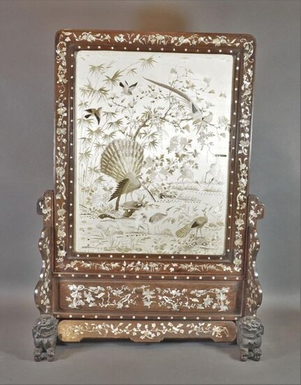 Screen composed of an embroidered silk panel decorated with peacocks, cranes and birds, the wooden frame inlaid with mother-of-pearl with lotus, bamboo and bat decoration. The wooden frame inlaid with mother-of-pearl decorated with characters and...